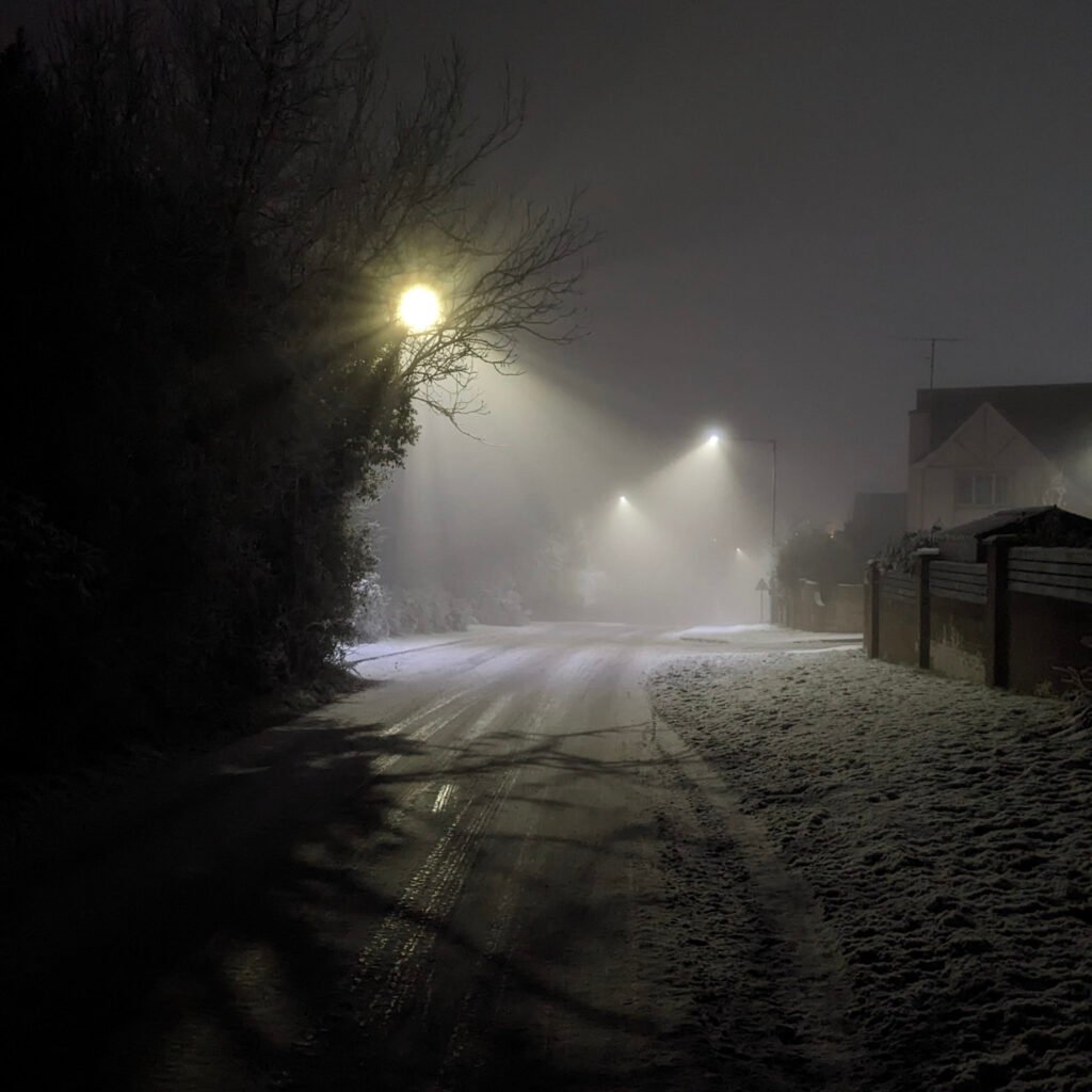 Ballinamullan road leading to Killyclogher road at night covered in snow with streetlights in fog